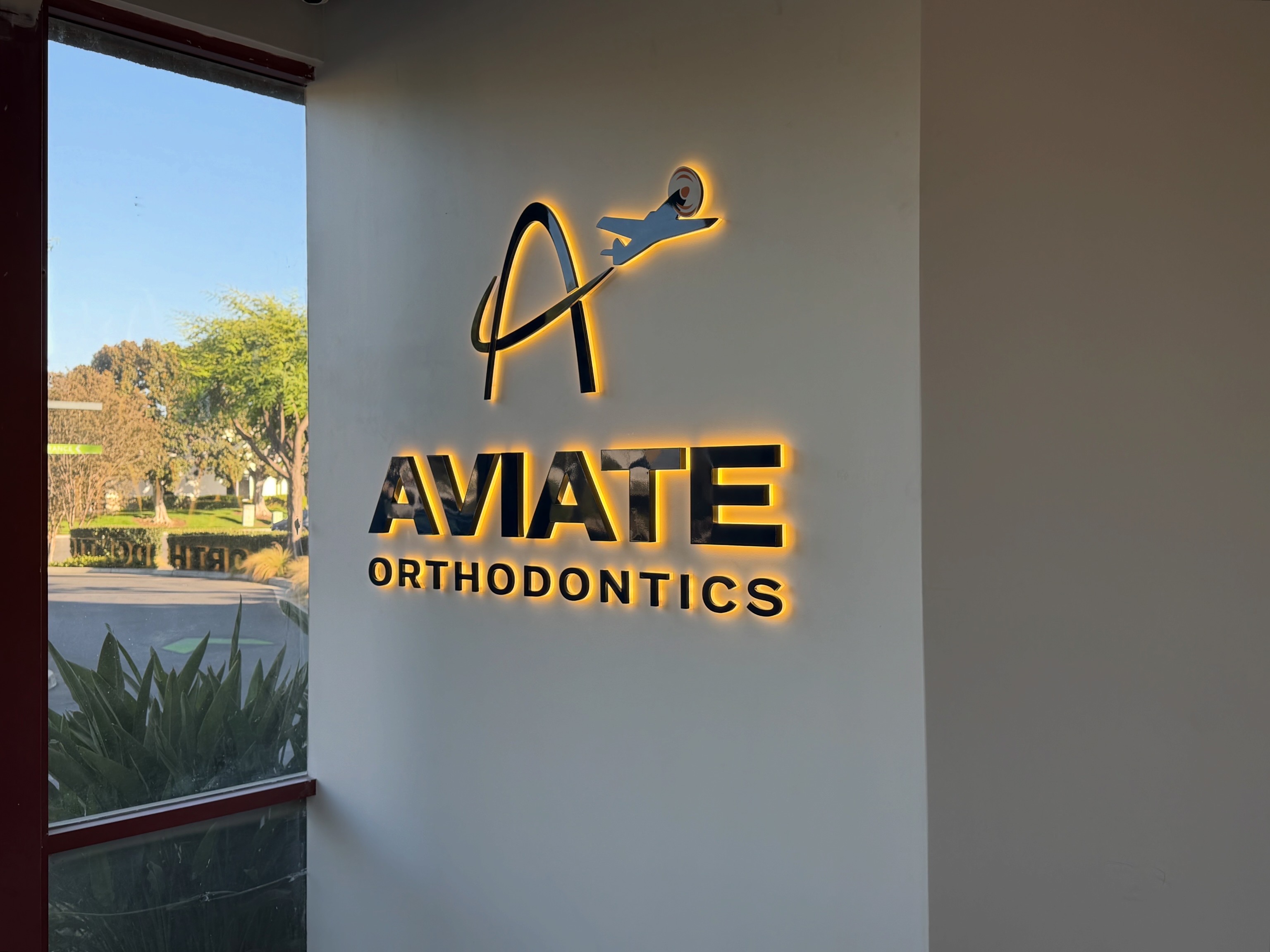 Warm halo-lit Aviate Orthodontics logo and letters beside a lobby window